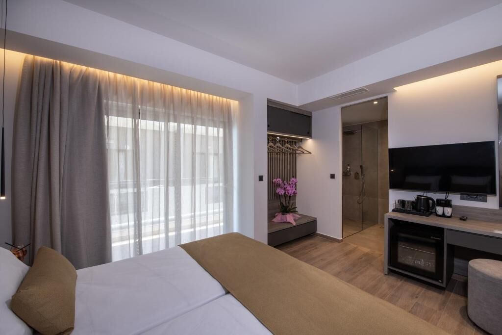 A modern hotel room with a bed, a desk with a flat-screen TV, a walk-in closet, and a bathroom.