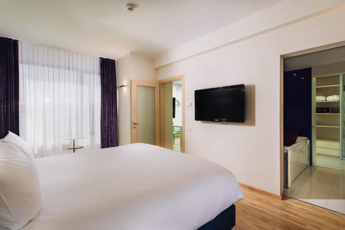 Une chambre d’hôtel avec un grand lit, un téléviseur fixé au mur et une porte-fenêtre coulissante donnant sur un balcon.