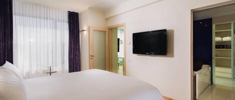 A hotel room with a large bed, a television mounted on the wall, and a sliding glass door leading to a balcony.