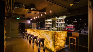 Un espace bar doté d’un comptoir en marbre, de tabourets et d’un bar bien garni de bouteilles.