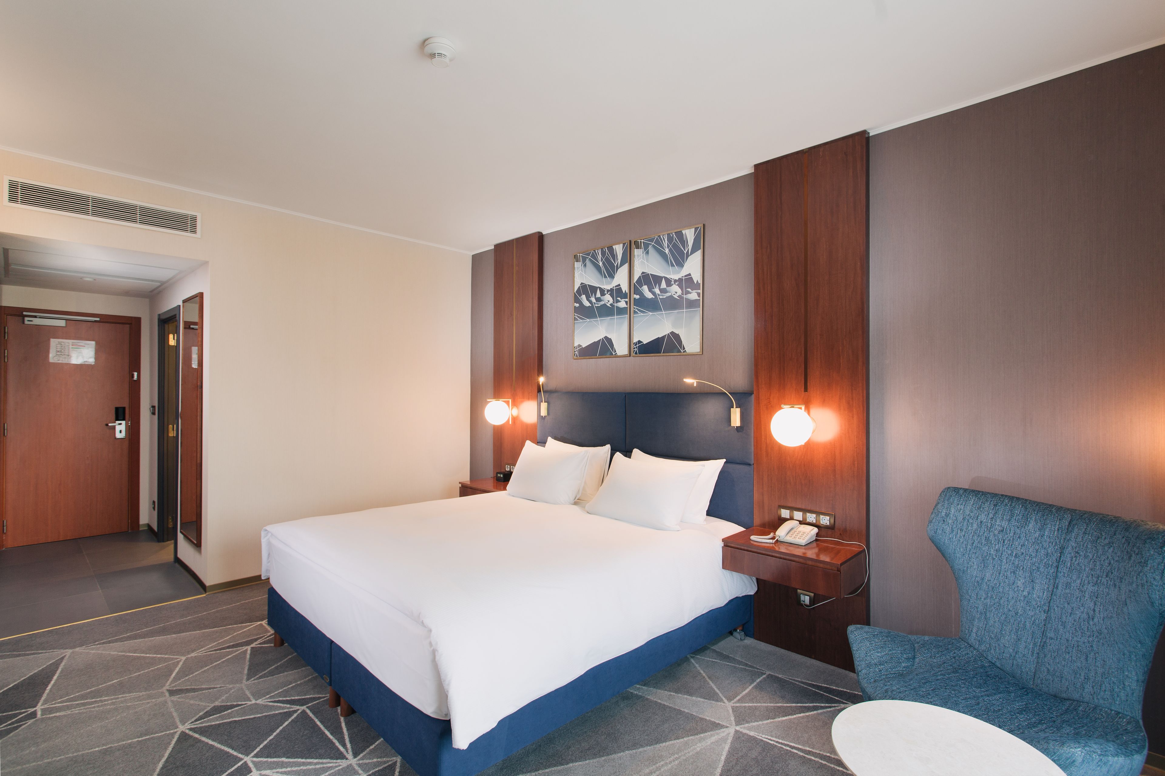 Une chambre d’hôtel avec un grand lit, une chaise bleue et un bureau avec un téléphone.