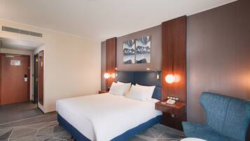 Quarto de hotel com uma cama grande, uma cadeira azul e uma escrivaninha com telefone.