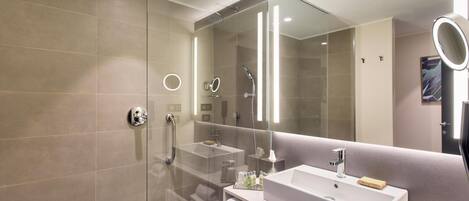 Un baño moderno con ducha envuelta en vidrio, un espejo grande y un tocador con lavamanos y toallero.