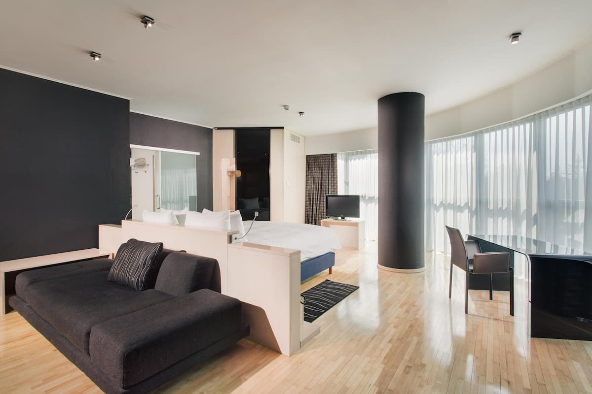 Une chambre d’hôtel moderne, équipée d’un lit, d’une table de chevet, d’une chaise et d’une grande fenêtre.
