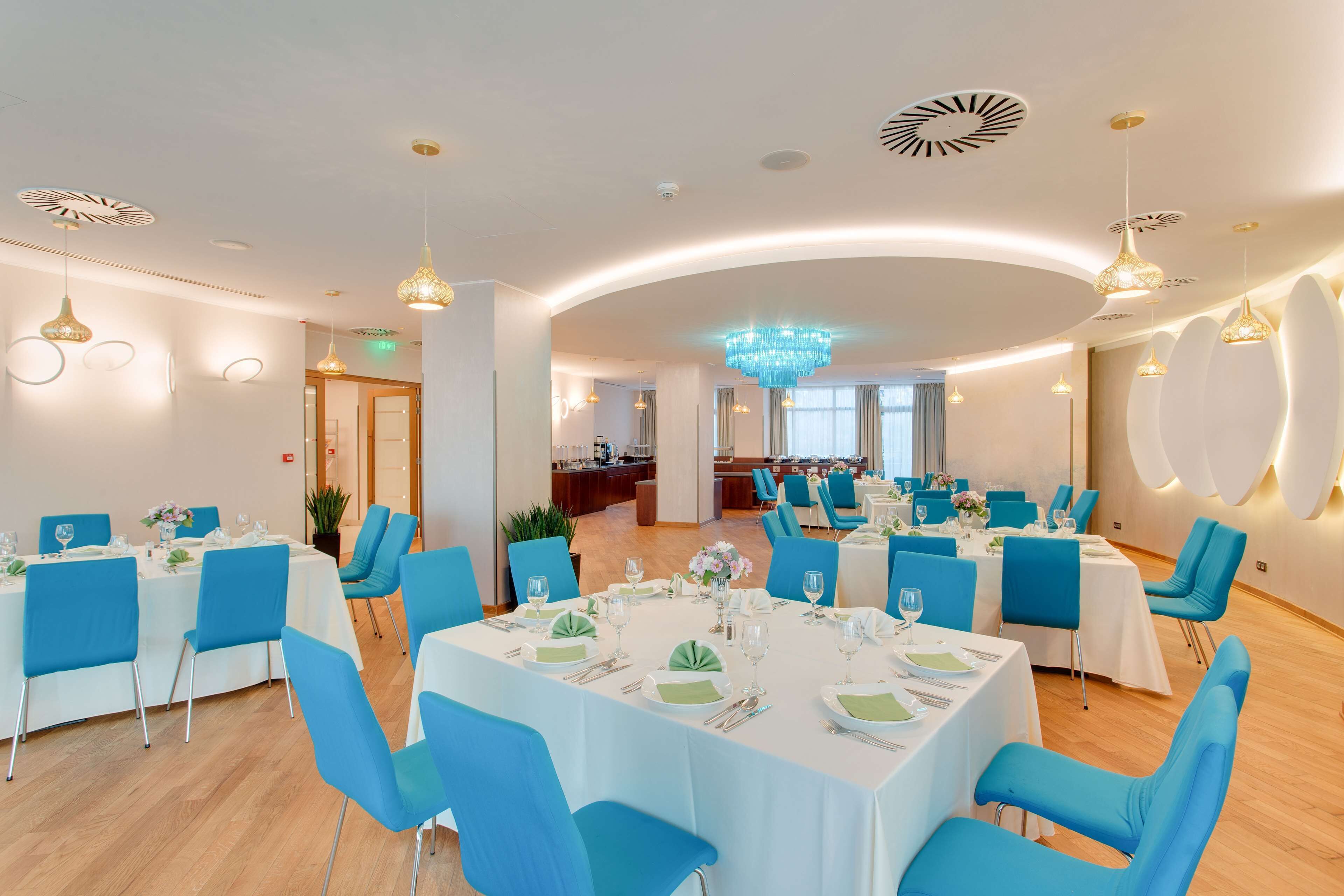 Comedor con mesas redondas, sillas azules y un candelabro.