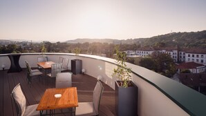 Une terrasse sur le toit, avec des tables et des chaises en bois, des plantes en pot et une vue sur le paysage urbain.