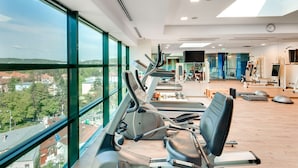 Une salle de sport équipée de matériel d’exercice, dotée de grandes fenêtres et offrant une vue sur la ville.