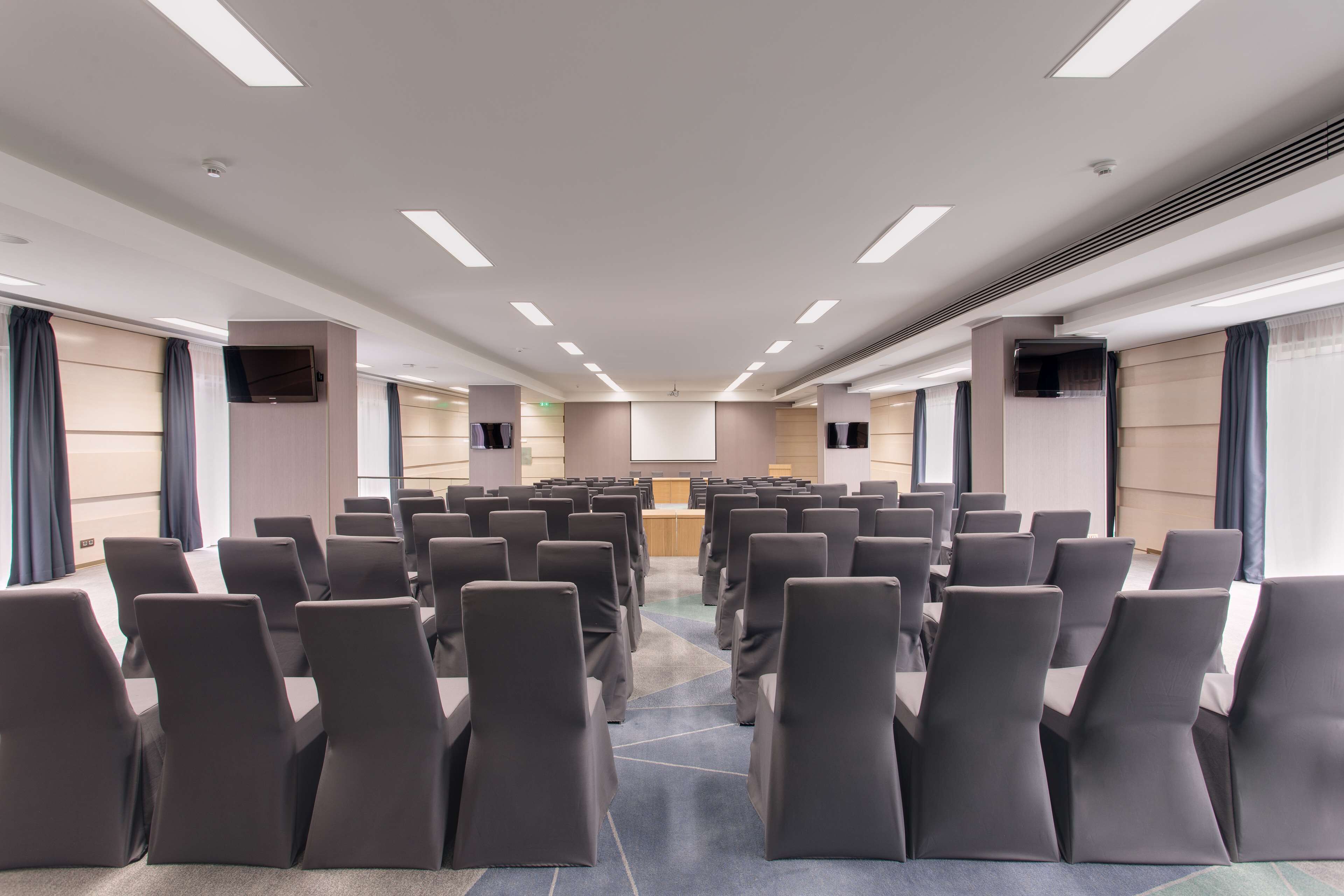 A conference room with rows of chairs, a podium, and a large screen at the front.