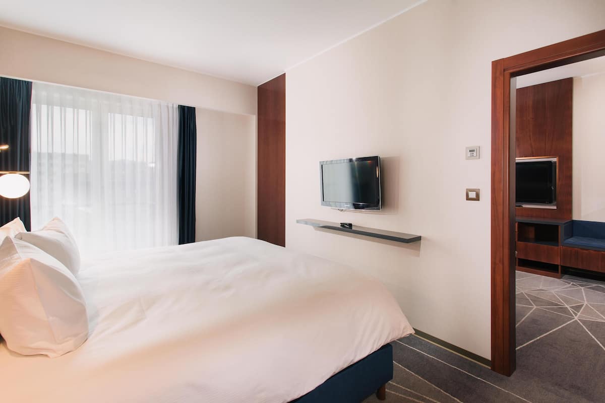 Une chambre d’hôtel avec un lit, un téléviseur fixé au mur, une porte en bois et une petite étagère.