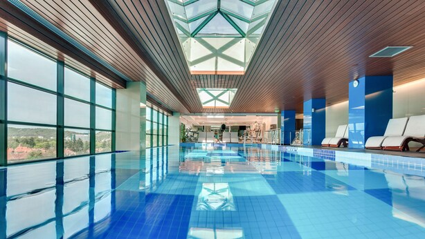 Une piscine dotée d’un plafond au design géométrique, de grandes fenêtres et offrant une vue sur les environs.