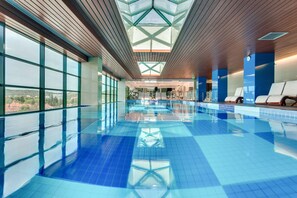 Una piscina con un diseño geométrico en el techo, amplios ventanales y vistas del entorno.