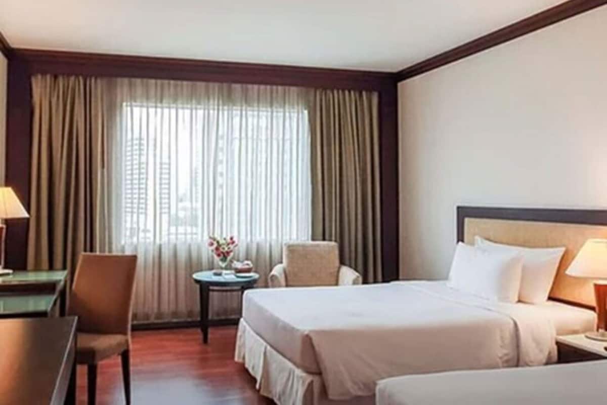 A hotel room with a bed, two chairs, a small table, and a window with curtains.