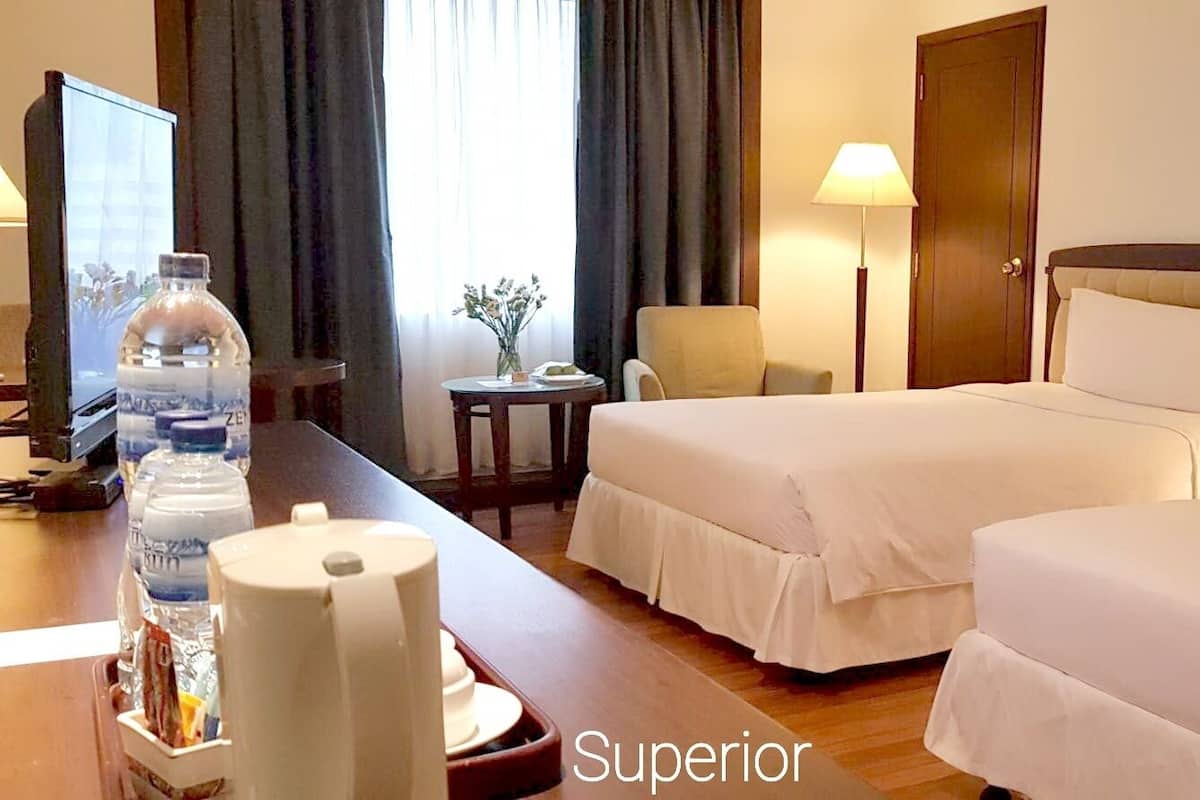 A hotel room with two beds, a desk with a water bottle and a lamp, and a door.