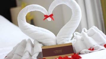 Une serviette pliée en forme de cygne, ornée d’un ruban rouge, une carte sur laquelle est inscrit « Hôtel Orchid » et quelques fleurs rouges éparpillées.