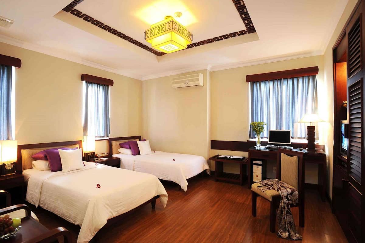 A hotel room with two beds, a desk with a computer, a chair, and a TV.