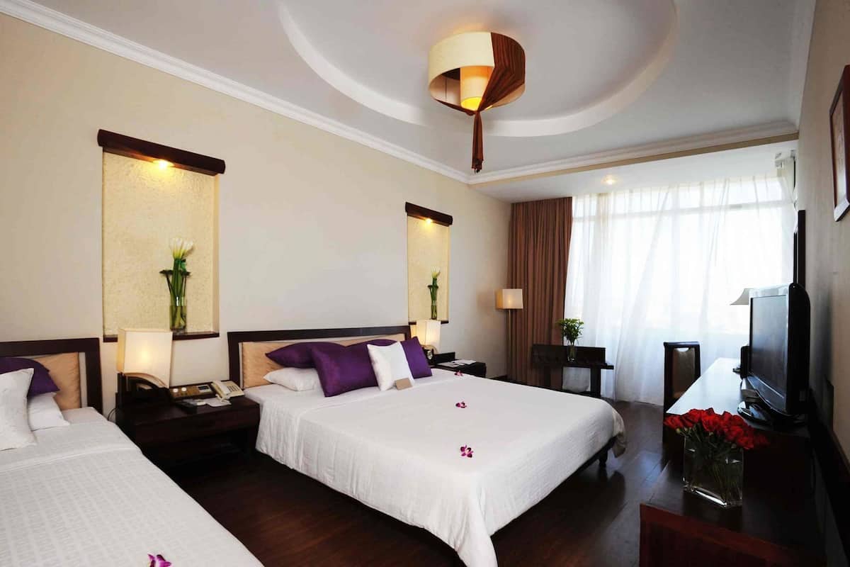 A hotel room with two beds, a TV, a desk with a computer, and a large window with curtains.