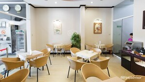 A restaurant with wicker chairs and tables, a kitchen area, and a clock on the wall. - Orchid Hotel (Hue)