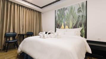 Habitación de hotel con una cama grande, un cuadro de plantas tropicales, un escritorio y dos sillas.