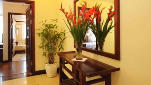 A hallway with a wooden console table, a potted bamboo plant, and a vase with red flowers. A mirror reflects the flowers and a bathroom in the background. - Orchid Hotel (Hue)