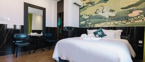 A hotel room with a bed, a desk, two chairs, a large mirror, and a wall with a nature-themed mural.
