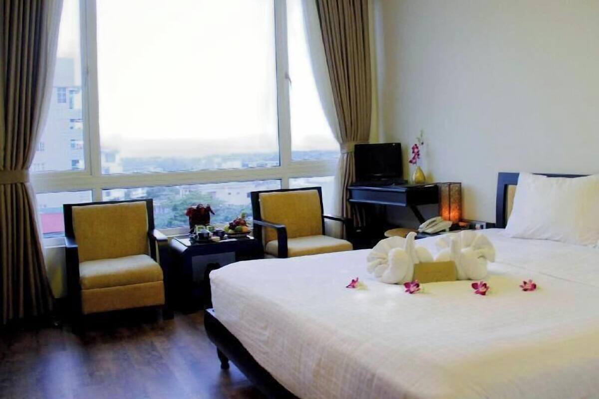 A hotel room with a bed, two chairs, a desk with a computer, a TV, and a city view.