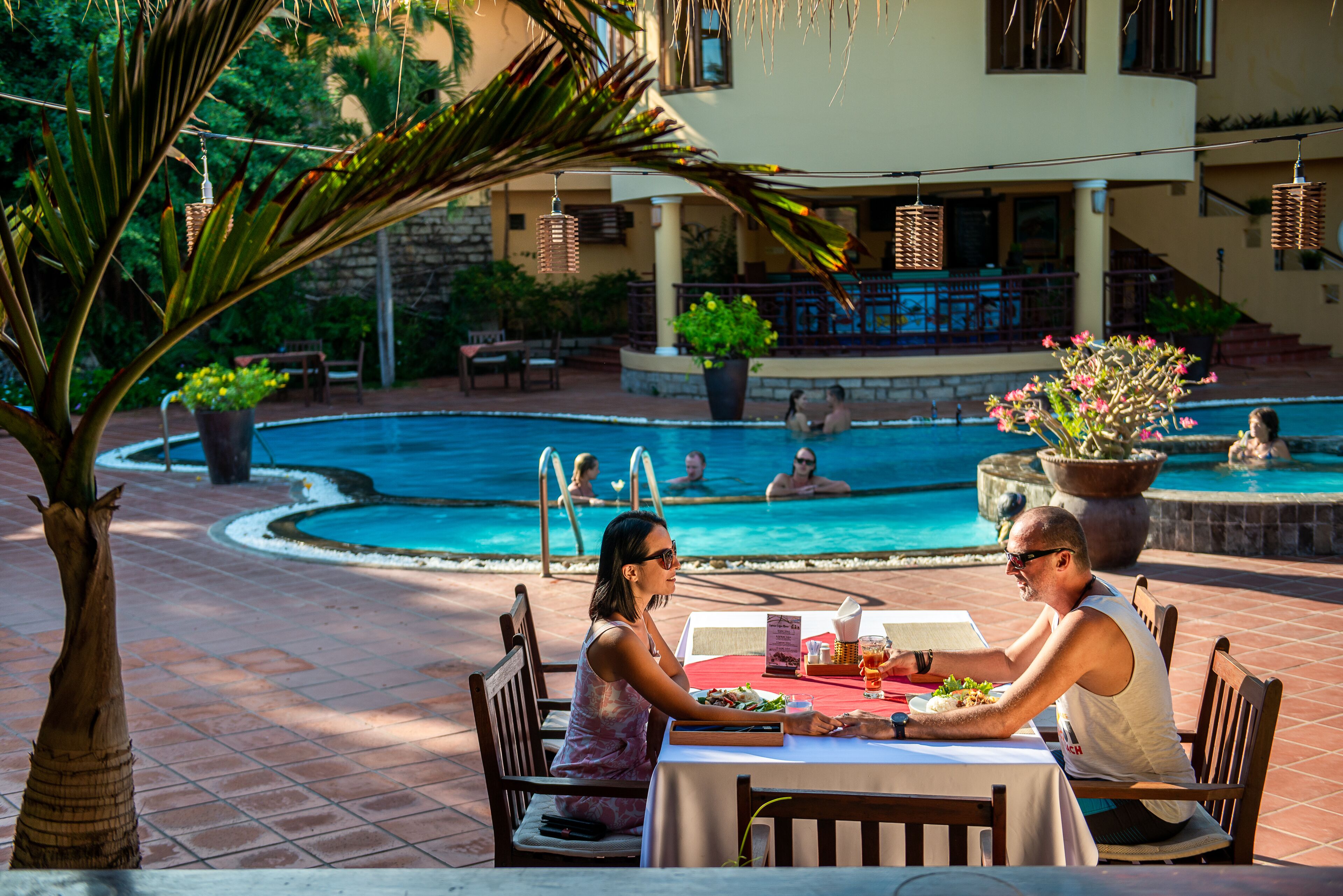 A dining area with a pool view, outdoor seating, and a stone wall backdrop.