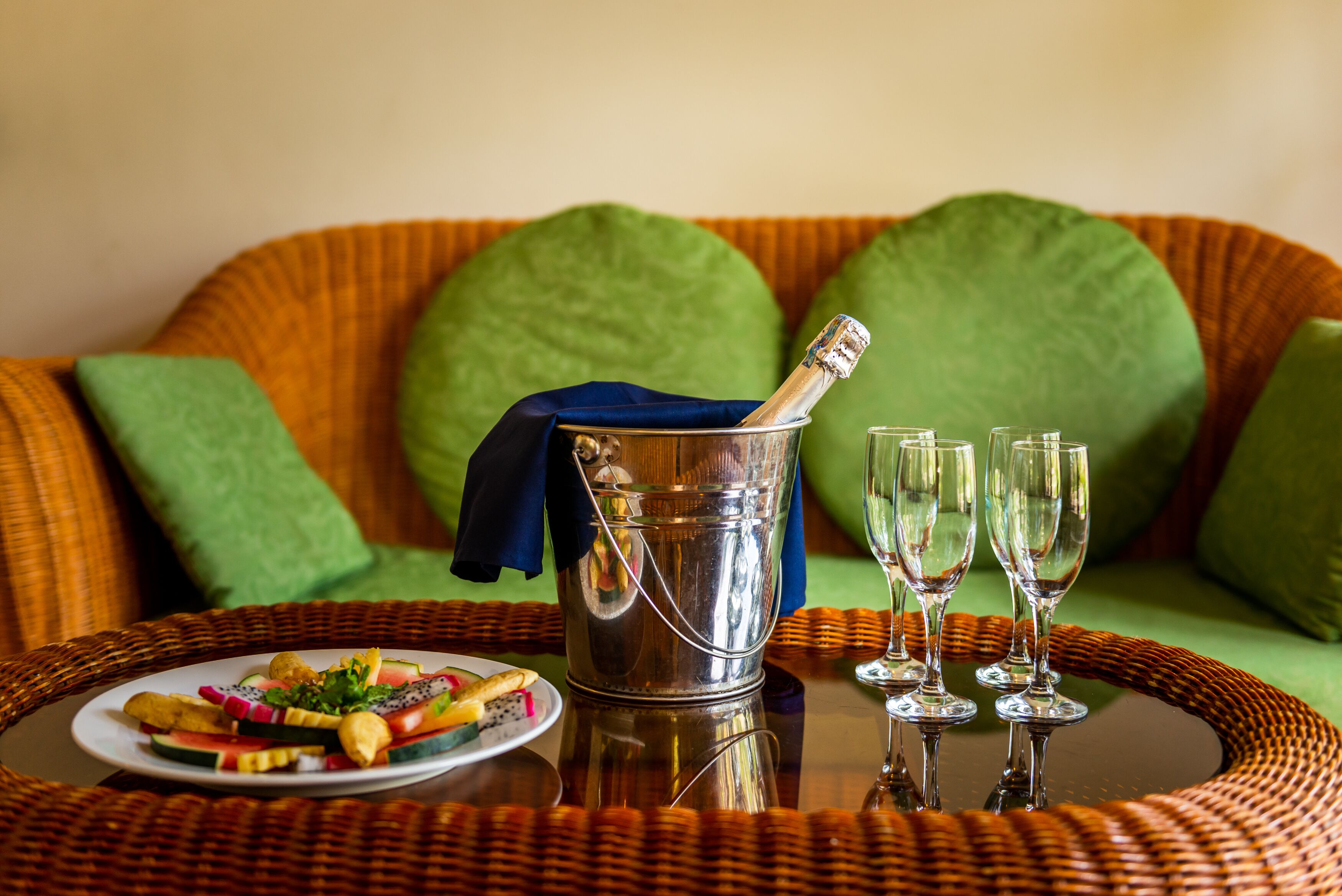 A wicker table with a metal bucket, three wine glasses, and a plate of fruit.