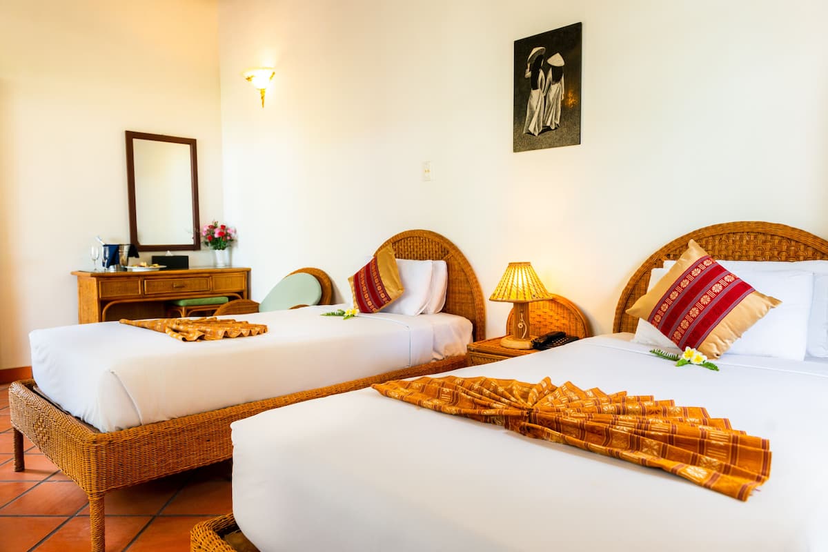 A hotel room with two single beds, a wooden nightstand with a lamp, a dresser, and a mirror.