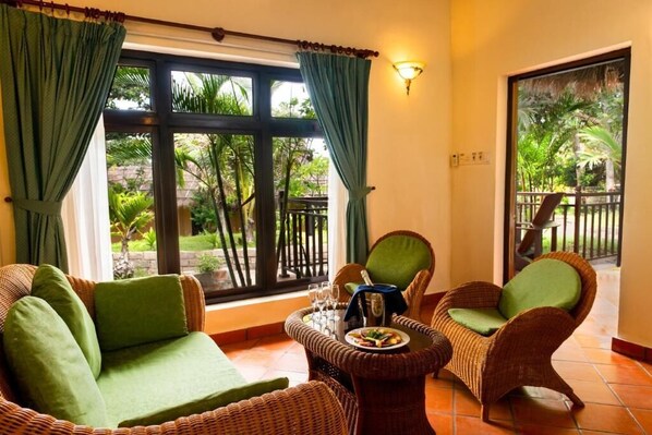 A room with wicker furniture, a dining table with a plate of food, and a view of greenery outside.