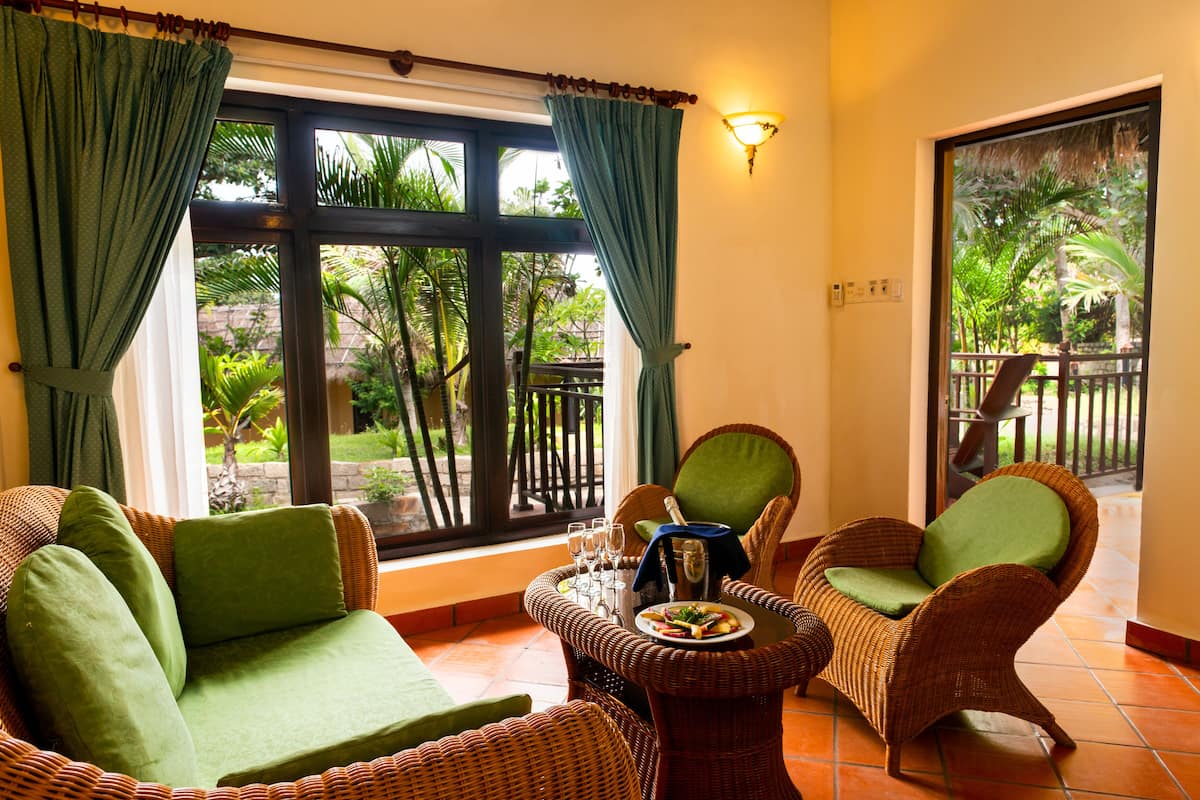 A room with wicker furniture, a dining table with glasses and a bottle, and a view of greenery outside.