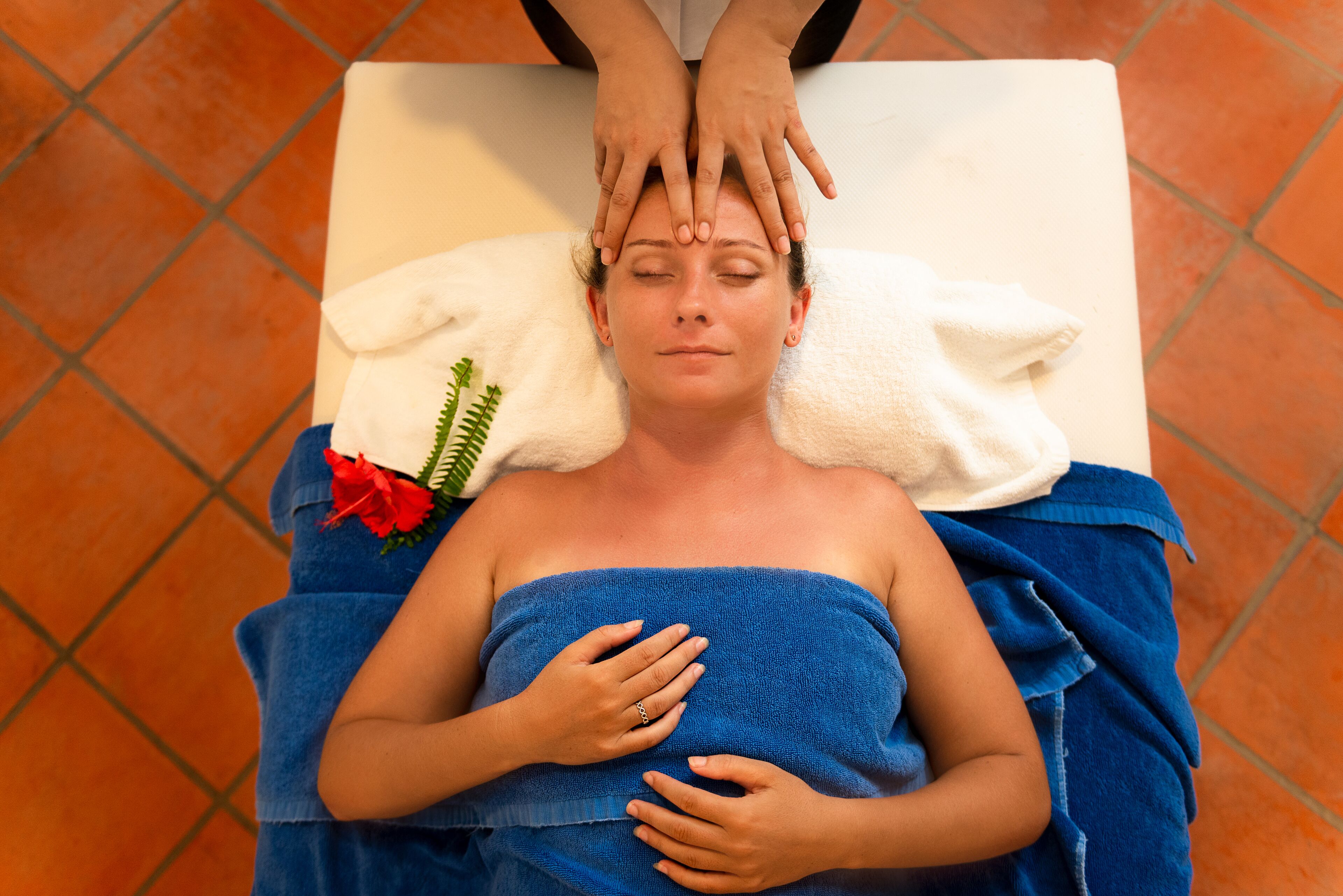 A person lying on a massage table with a towel wrapped around their body, receiving a head massage.