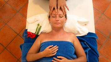 A person lying on a massage table with a towel wrapped around their body, receiving a head massage.
