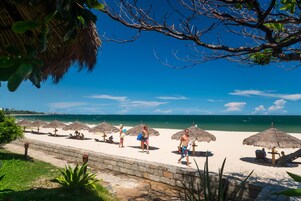 A beach with thatched umbrellas, a stone wall, and the ocean in the background.