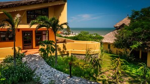 A yellow building with a thatched roof, surrounded by lush greenery and a clear view of the ocean. - White Sand Resort (Phan Thiet)