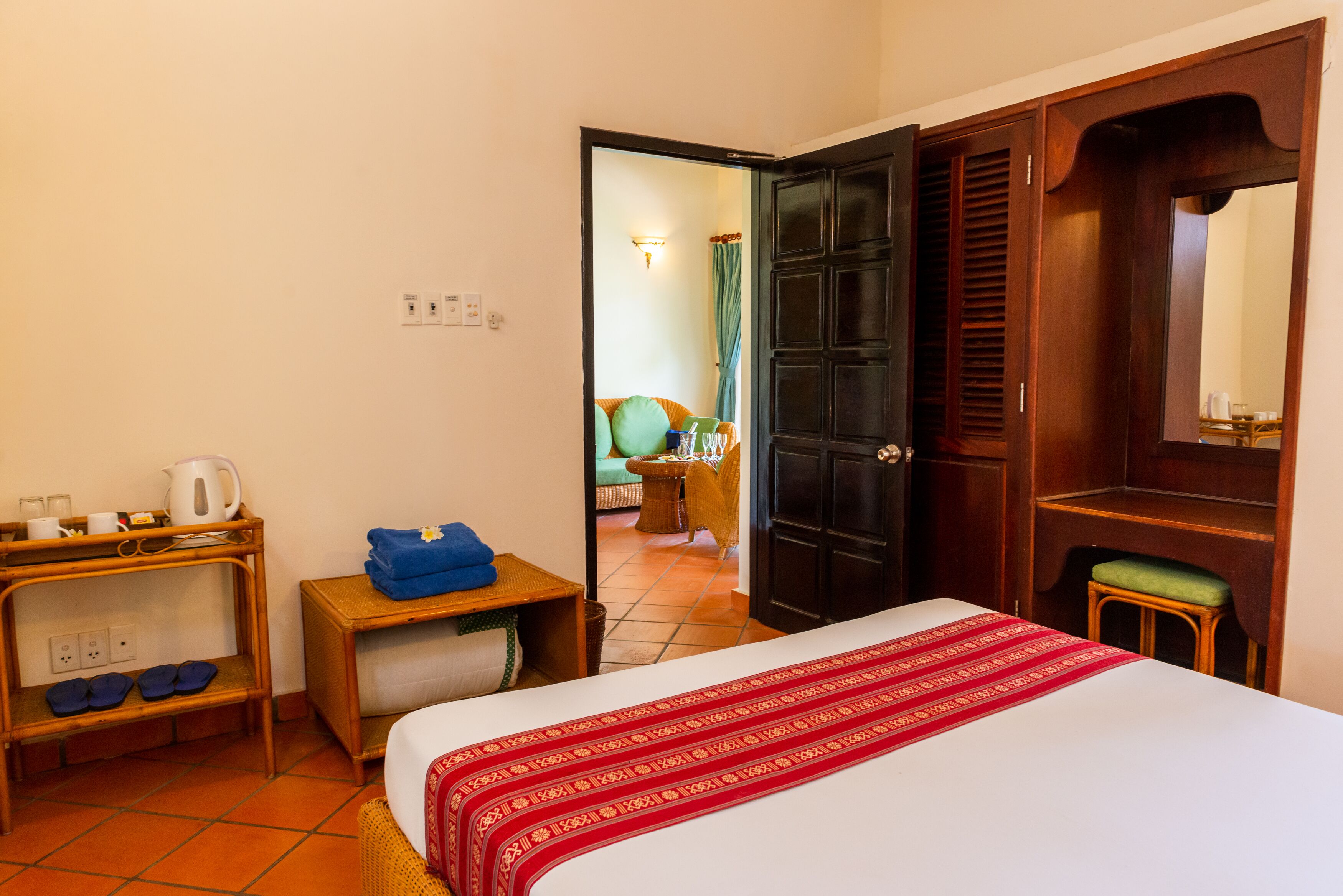 Une chambre d’hôtel avec un lit, une armoire en bois, une petite table avec une bouilloire et des tasses, et une chaise.
