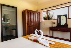 Habitación de hotel con cama, armario de madera, baño con lavamanos y espejo, y ventana con vista a árboles.