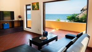 A living room with a TV, a sofa, a dining table with a plate of food, and a balcony with a view of the sea. - White Sand Resort (Phan Thiet)