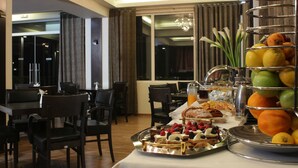 Un área de comedor con una mesa de buffet que ofrece diversos pasteles, frutas y una presentación de frutas.