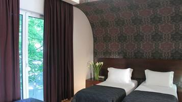 Hotelkamer met twee bedden, een groot raam met gordijnen, een kamer met patroon en een kleine tafel met een bloevas.