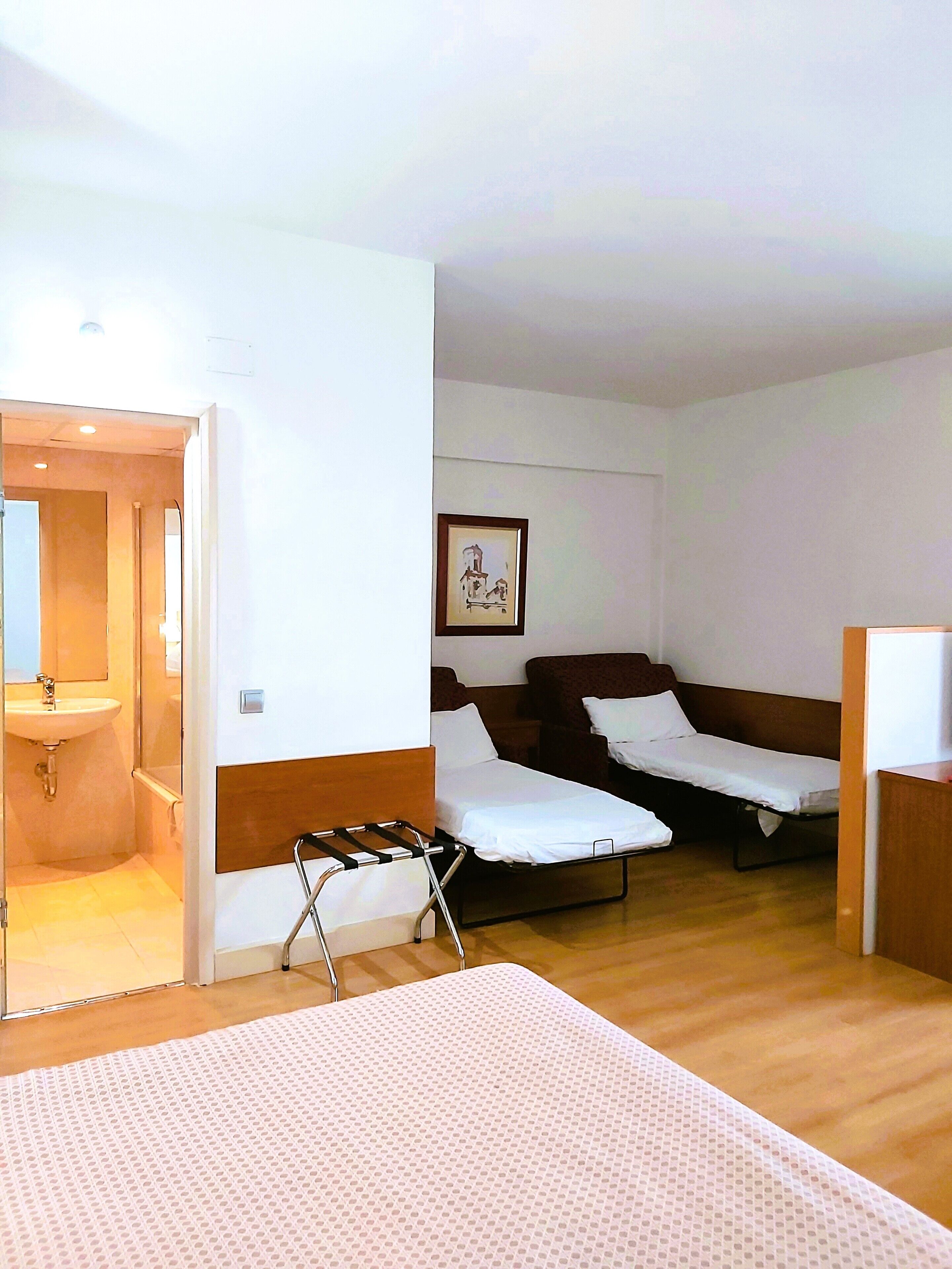 A hotel room with a bed, a small sofa, a bedside table, and a bathroom with a sink and mirror.