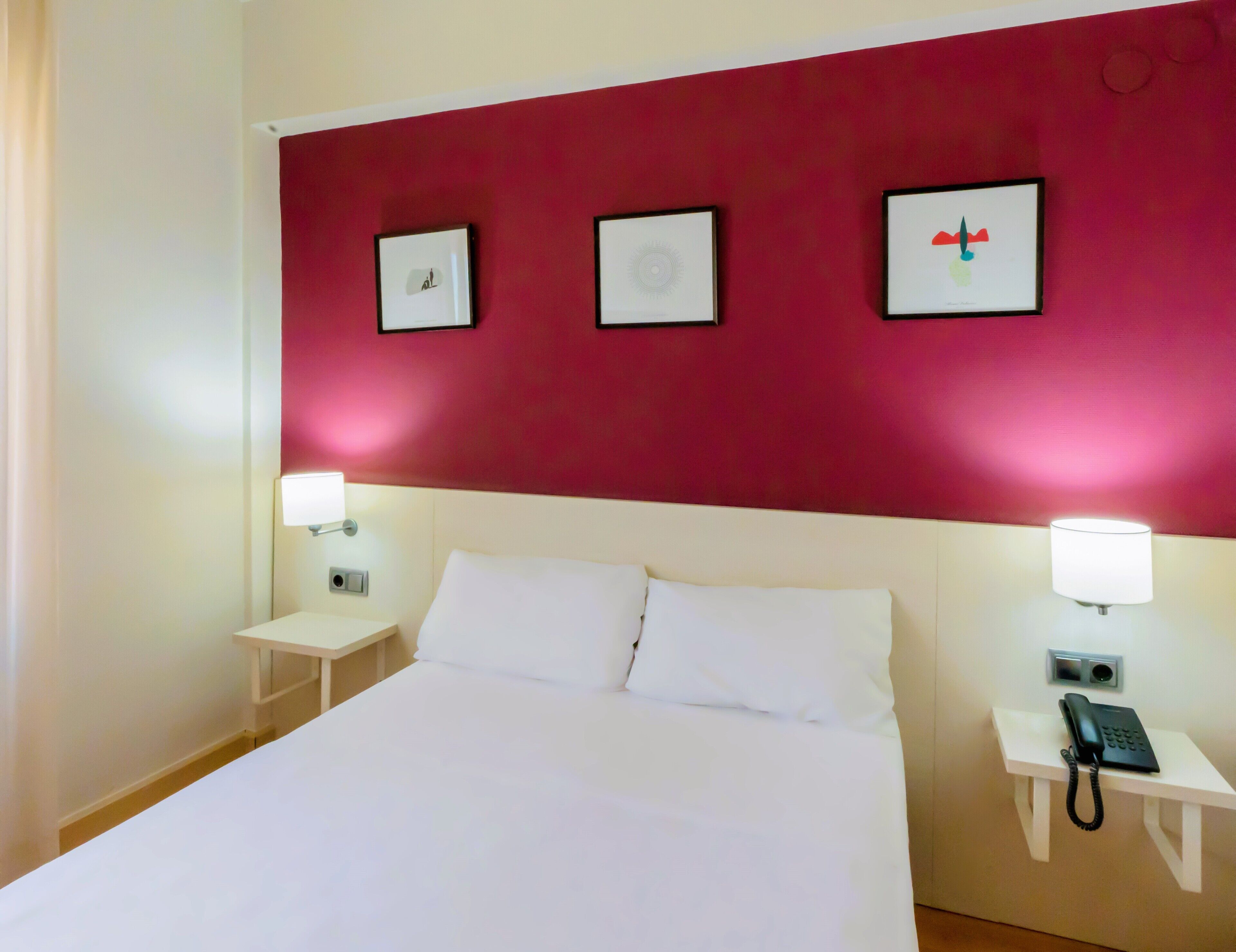A hotel room with a large bed, two bedside tables with lamps, and three framed pictures on the wall.