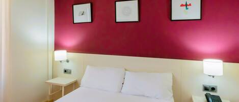 Habitación de hotel con una cama grande, dos mesitas de noche con lámparas y tres cuadros enmarcados en la pared.