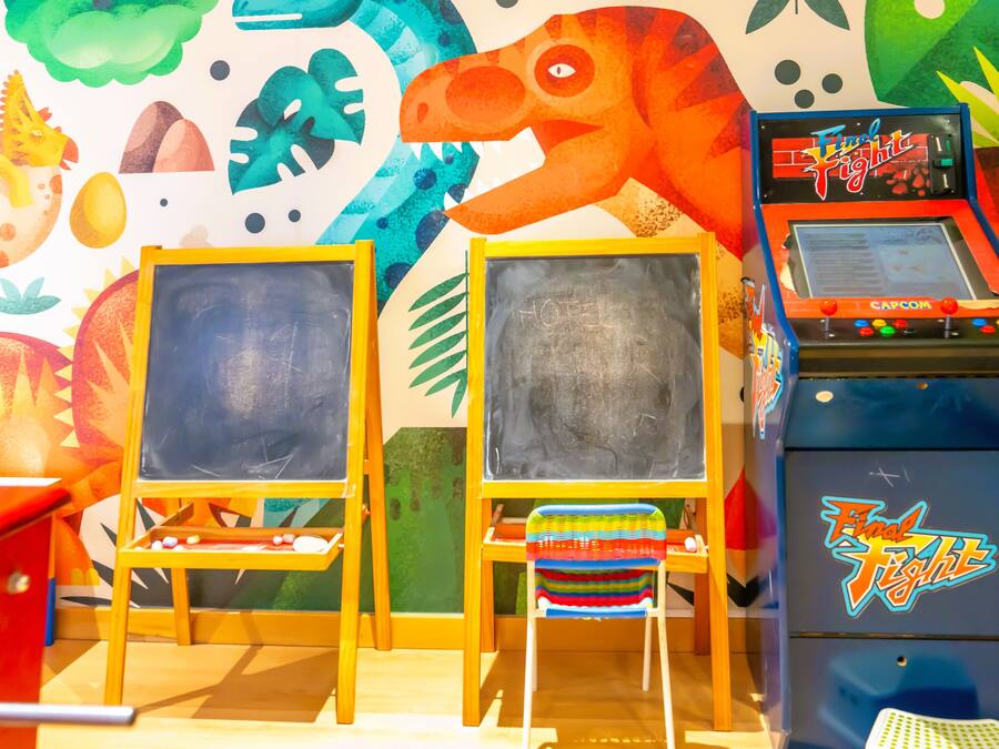 Two chalkboards on easels, a colorful dinosaur mural, and a 'Final Fight' arcade machine.