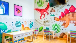 Une salle de jeux pour enfants avec des peintures murales colorées, des meubles en bois et un téléviseur.