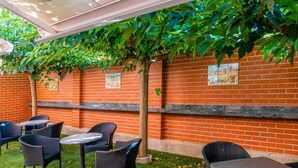 Un espace extérieur aménagé en terrasse, avec des murs en briques, un décor de plantes artificielles vertes et des meubles en osier.