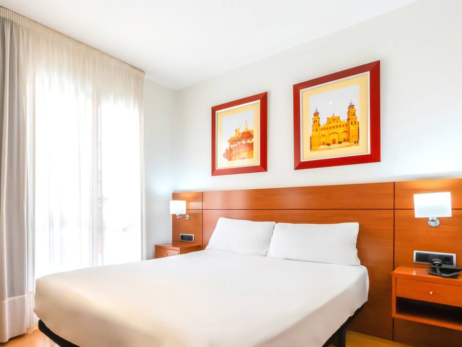A hotel room with a large bed, two bedside tables, a nightstand, and two framed pictures on the wall.