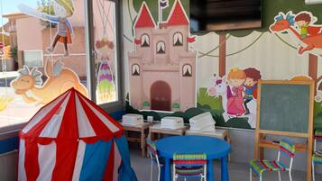 A children's playroom with a tent, tables, chairs, and educational murals.
