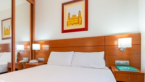 Une chambre d’hôtel avec un grand lit, deux tables de chevet, une petite table avec une lampe, un tableau encadré au mur et un miroir.