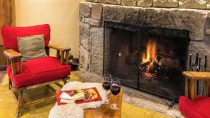 A cozy room with a fireplace, a red armchair, a wooden table with food and wine glasses.