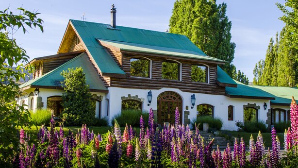 A log cabin with a green roof, arched windows, and a stone entrance.